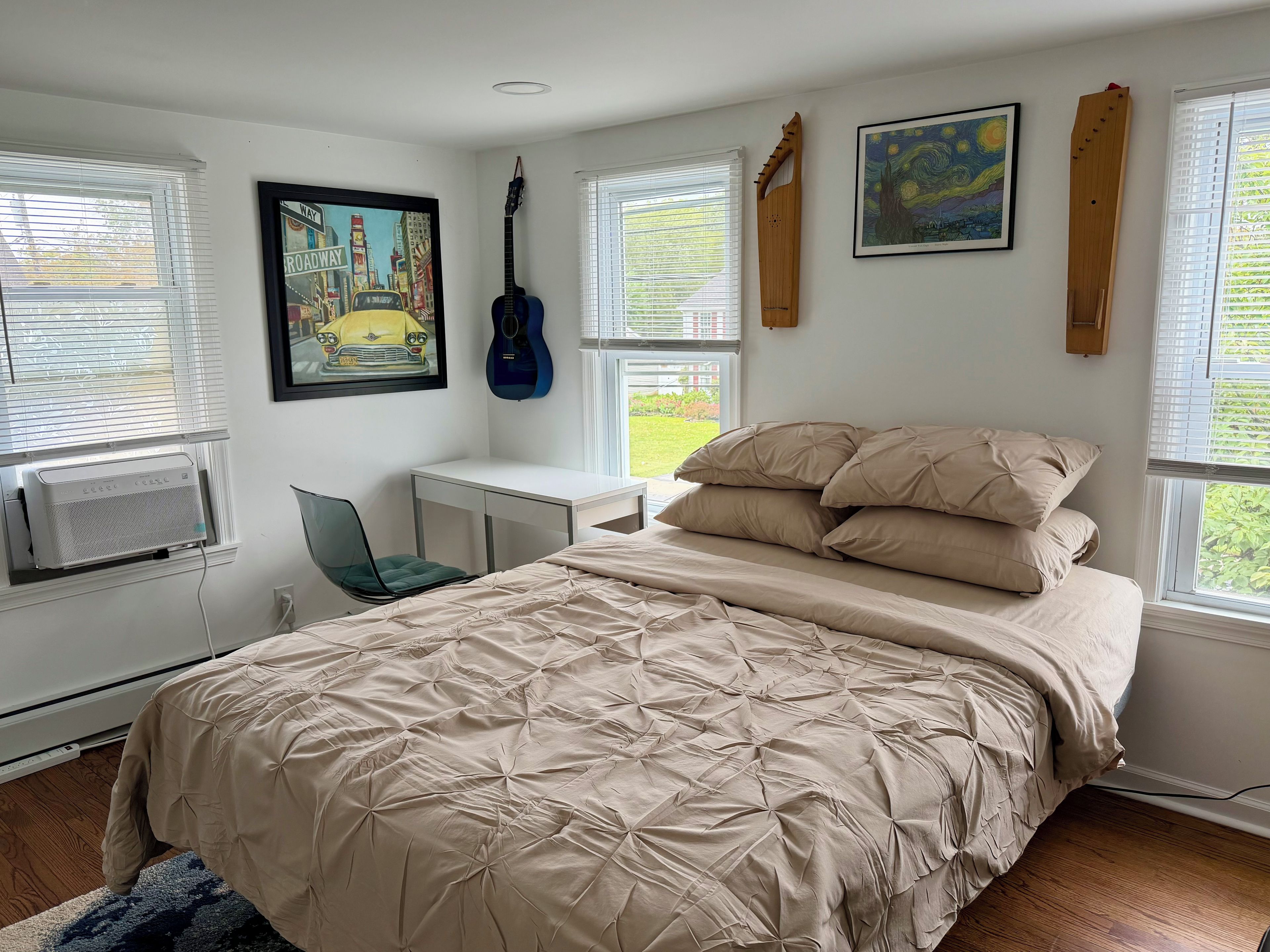 Une chambre à coucher avec un lit, un bureau, une chaise, une guitare et des œuvres d’art accrochées aux murs.