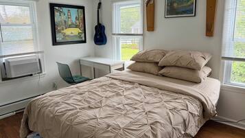 Une chambre à coucher avec un lit, un bureau, une chaise, une guitare et des œuvres d’art accrochées aux murs.
