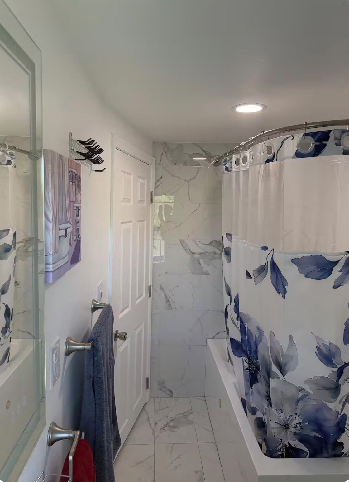 A bathroom with a shower, a glass-enclosed shower area, a marble-tiled floor, and a shower curtain with a floral pattern.