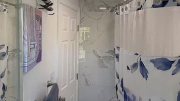 A bathroom with a shower, a glass-enclosed shower area, a marble-tiled floor, and a shower curtain with a floral pattern.