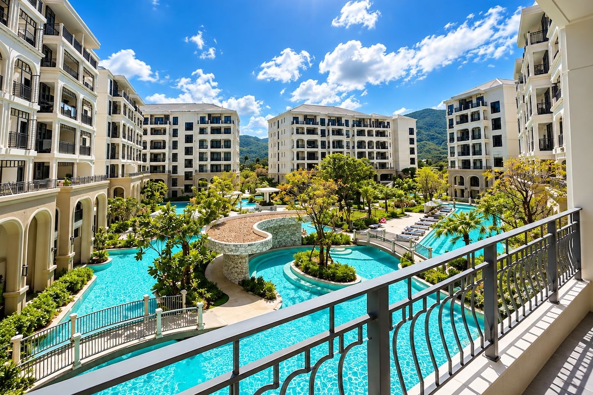 A multi-story hotel with a central swimming pool surrounded by lush greenery and multiple balconies.