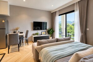 A modern hotel room with a bed, a desk, a television, and a balcony with a view. - Title Legendary Apartment by TVC (Tambon Choeng Thale)