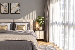 A modern bedroom with a bed, bedside tables, and a large window with curtains. - Title Legendary Apartment by TVC (Tambon Choeng Thale)