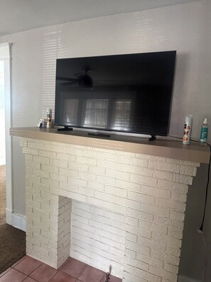 A flat-screen TV mounted on a white brick fireplace mantel with a remote control. -  Spacious 3BR Retreat Minutes from Water & Downtown (Erie)