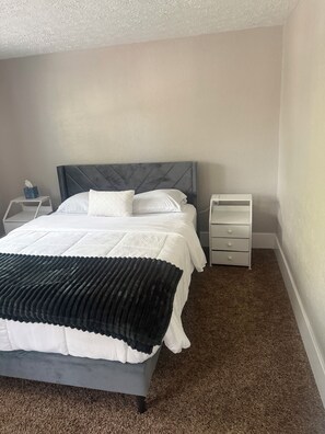 A neatly made bed with a dark headboard, a white bedside table with a tissue box, and a white nightstand with drawers. -  Spacious 3BR Retreat Minutes from Water & Downtown (Erie)