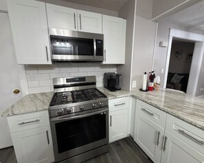 A kitchen with white cabinets, a stainless steel stove, a microwave, and a coffee maker. -  Spacious 3BR Retreat Minutes from Water & Downtown (Erie)