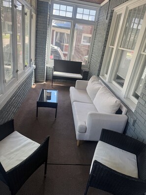 A sunlit patio with a white sofa, two wicker chairs, and a small table. -  Spacious 3BR Retreat Minutes from Water & Downtown (Erie)