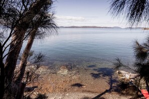 A clear view of a lake with a rocky shoreline and trees framing the scene. - 'Lazy Susan's' Waterfront Shack (Primrose Sands)