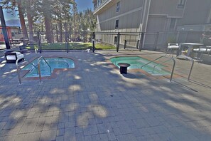 A pool area with two pools, a covered seating area, and a building in the background. - Updated Ski-in/ski-out 2BR condo,mntn vws, 3 hot tubs,1 summer pool,arcade games located in 1849  #107 (Mammoth Lakes)
