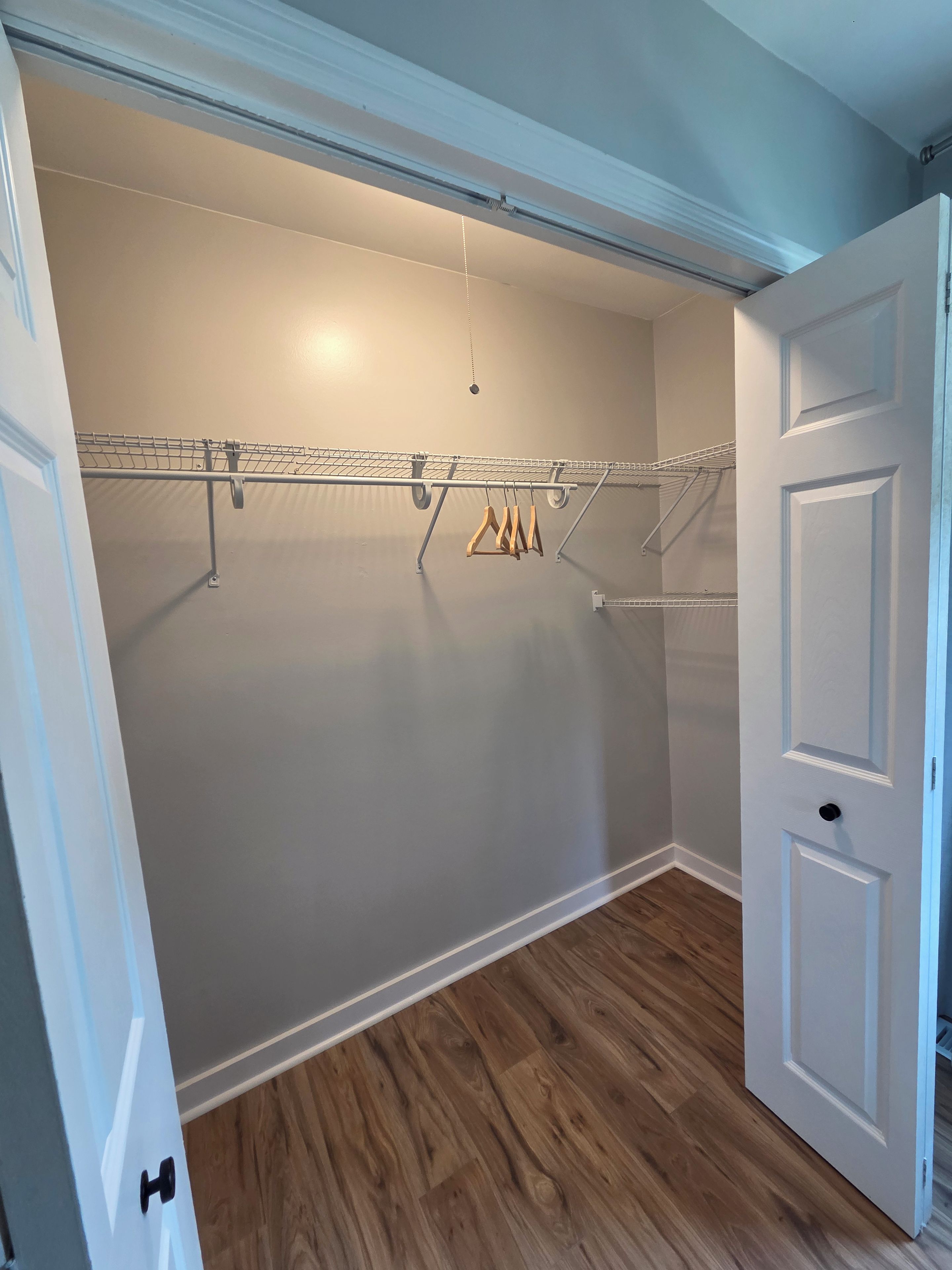 A walk-in closet with a metal drying rack, wooden hangers, and a door.