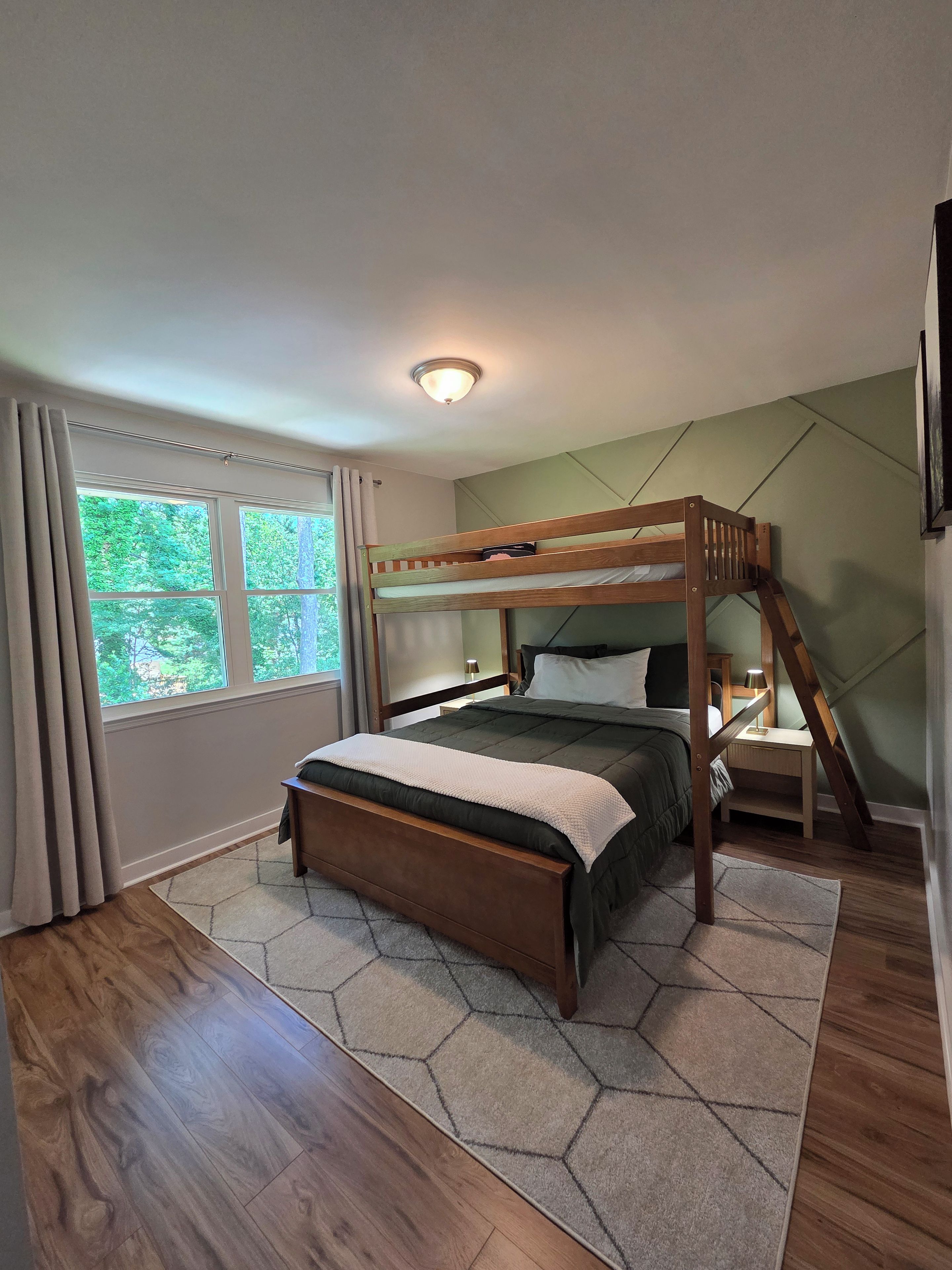 A room with a bunk bed, a desk, a nightstand, a window with curtains, and a ceiling light.