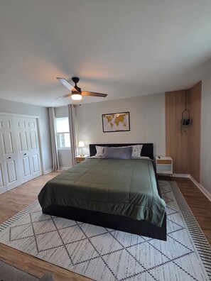A bedroom with a bed, a ceiling fan, a world map on the wall, and a nightstand with a lamp. - Stylish renovated 2BR - 5 min drive to Truist Park (Smyrna)