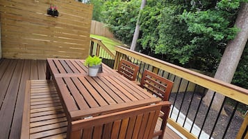A wooden deck with a table and chairs, surrounded by a wooden fence and trees.