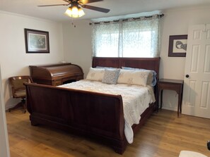 Un dormitorio con una cama de madera, un escritorio con un piano, un ventilador de techo y una puerta.