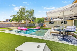 Patio trasero con piscina, sillas de descanso y una mesa con toallas y bebidas.
