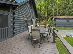 A wooden deck with a table and chairs, surrounded by a forested area. - Fox Hollow - Pet Friendly | Hot Tub | Firepit | Game Room (Blue Ridge)