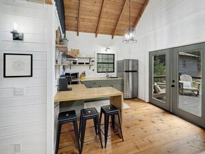 A modern kitchen with a wooden island, bar stools, a stainless steel refrigerator, and a large sliding glass door leading to an outdoor patio. - Fox Hollow - Pet Friendly | Hot Tub | Firepit | Game Room (Blue Ridge)
