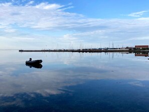 Ruhige Wasserfläche mit einem Boot, eine Pier mit mehreren Booten und ein Gebäude im Hintergrund.