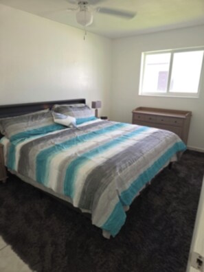 A bedroom with a bed, a ceiling fan, a nightstand, a dresser, and a window. - Entire 2/1 Rental Unit in Fort Lauderdale (Lauderhill)