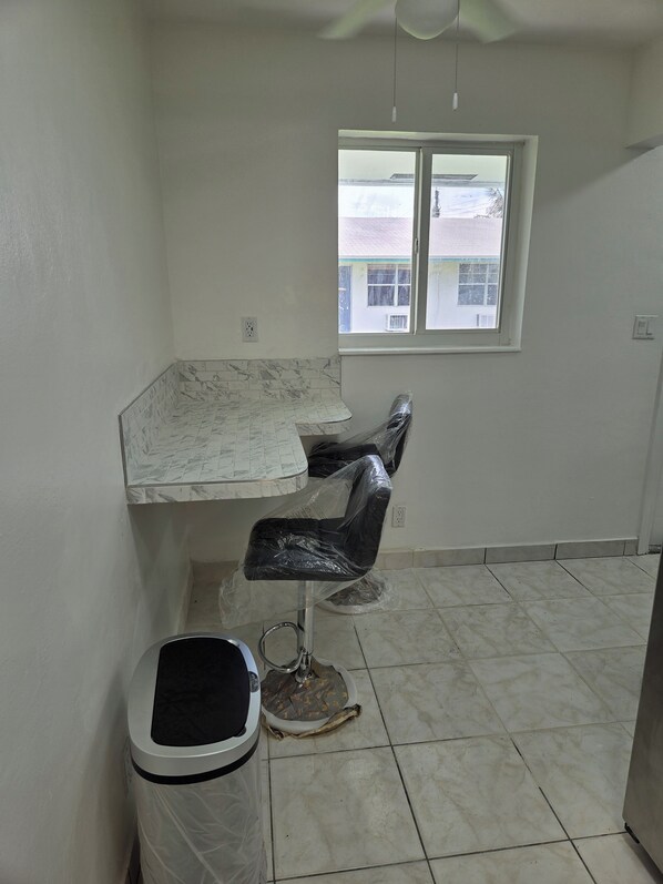 A room with a tiled floor, a window with a view, a chair, and a trash bin.