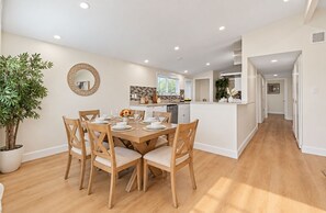 A modern kitchen with white cabinets, a dining area with wooden chairs, and a potted plant. - Cozy 4BR Home Near Disneyland & Anaheim CC Sleep 15 (Anaheim)
