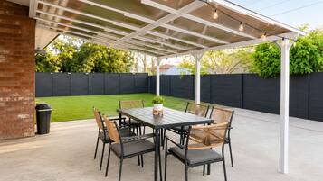 A covered patio with a table and chairs, a potted plant, and a brick wall.