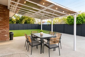 A covered patio with a table and chairs, a potted plant, and a brick wall. - Cozy 4BR Home Near Disneyland & Anaheim CC Sleep 15 (Anaheim)