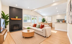 A modern living room with a fireplace, a sofa, a coffee table, and a dining area. - Cozy 4BR Home Near Disneyland & Anaheim CC Sleep 15 (Anaheim)