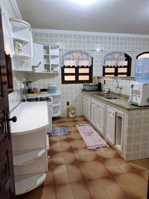 A kitchen with white cabinets, a stove, a sink, and a water dispenser. - Cozy family home where you can have good conversation and good food, good conversation and the beach. (Armação dos Búzios)