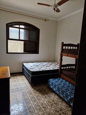 A room with a bunk bed, a window with blinds, a ceiling fan, and patterned floor tiles. - Cozy family home where you can have good conversation and good food, good conversation and the beach. (Armação dos Búzios)