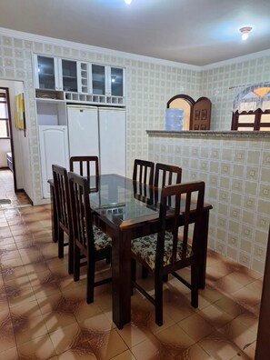 A dining area with a glass-top table surrounded by wooden chairs with cushioned seats. - Cozy family home where you can have good conversation and good food, good conversation and the beach. (Armação dos Búzios)