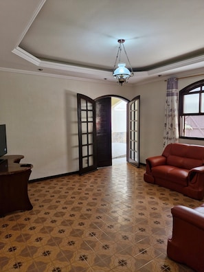 A room with a patterned floor, a sofa, a television on a stand, and a ceiling fan. - Cozy family home where you can have good conversation and good food, good conversation and the beach. (Armação dos Búzios)