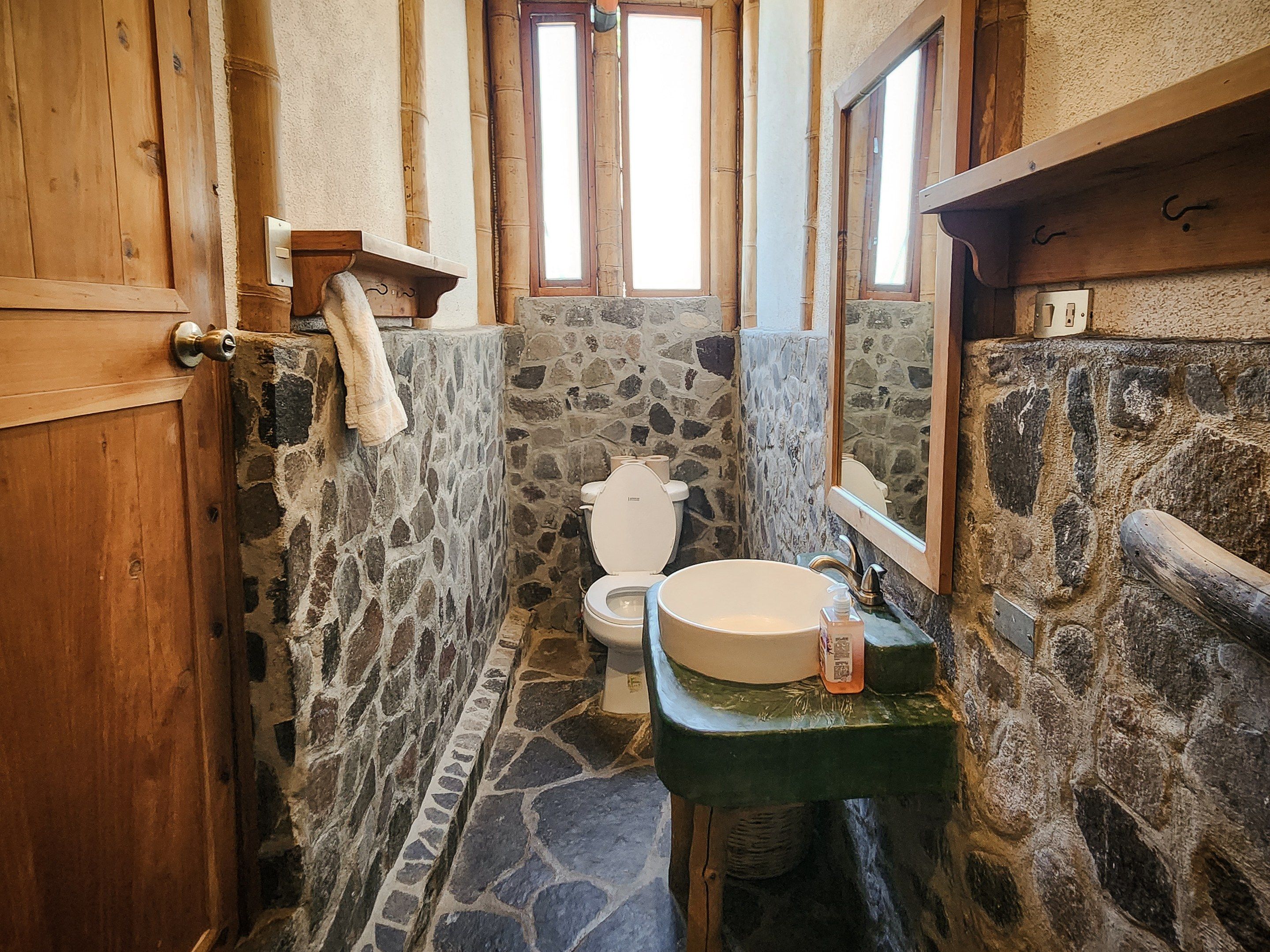 Un baño con pared de piedra, puerta de madera y lavamanos verde.