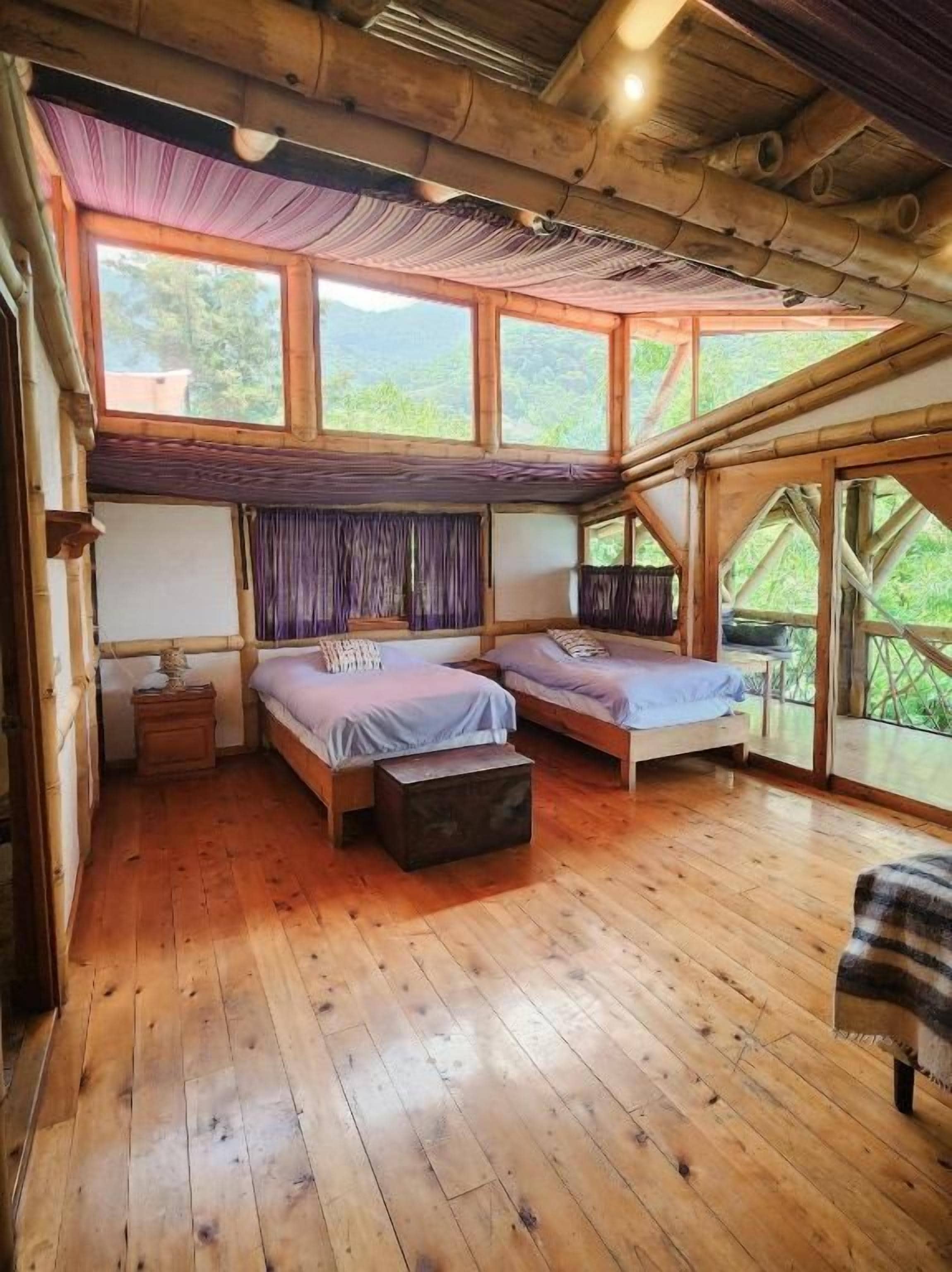 Une chambre avec deux lits, un plancher en bois et de grandes fenêtres.