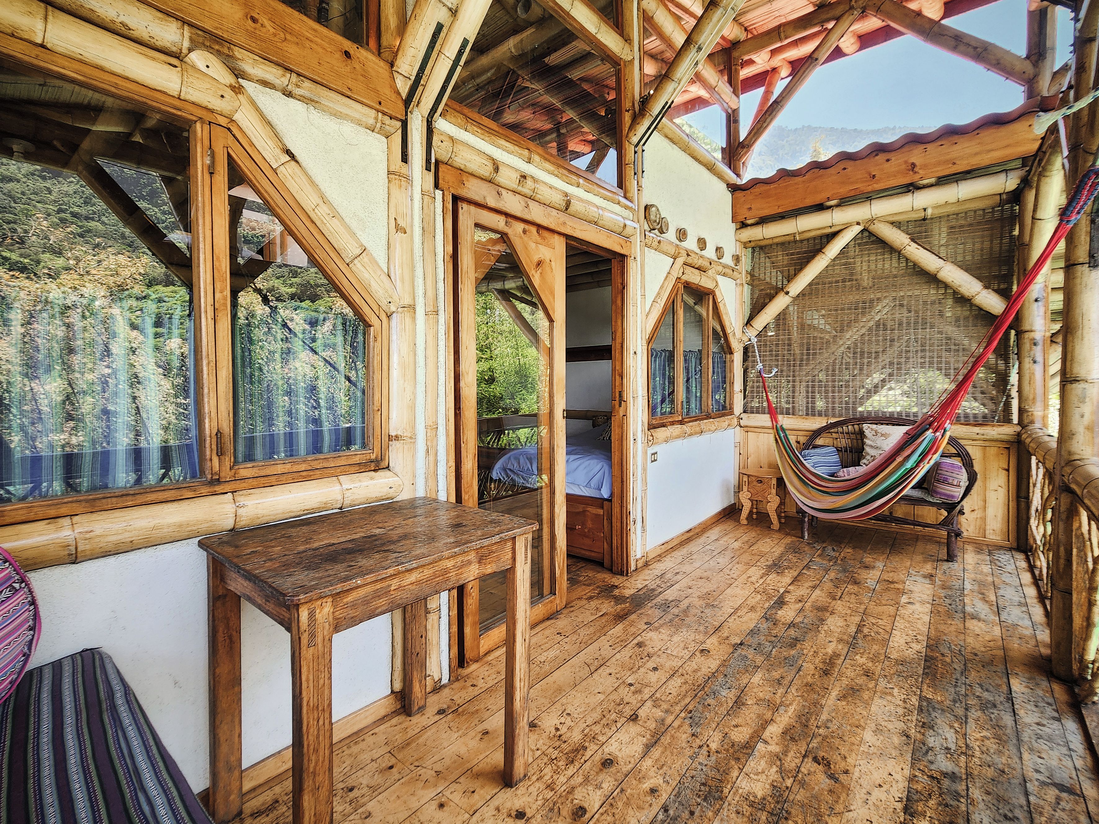 A wooden cabin with a hammock, a table, and a view of the forest.