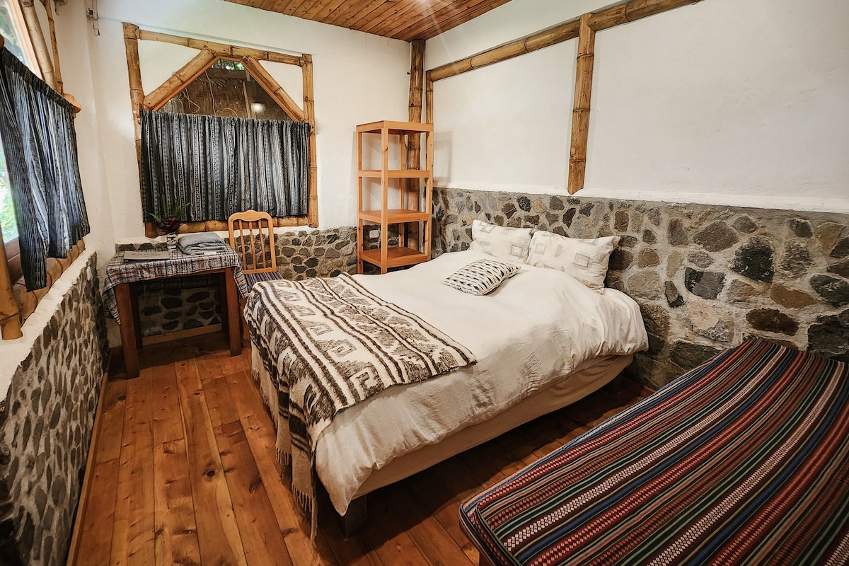 Un dormitorio con pared de piedra, cama de madera y una pequeña mesa con una silla.