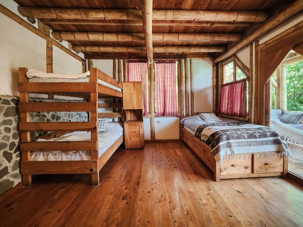 A rustic wooden room with bunk beds, a small table, and a window with curtains.