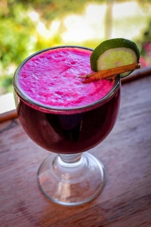 Un vaso con una bebida rosada, adornado con una rodaja de limón y una rama de canela, sobre una superficie de madera.