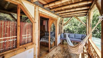 A wooden structure with a covered porch, a hammock, and a bed with pillows.