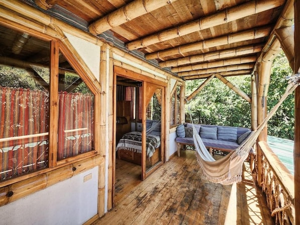A wooden structure with a covered porch, a hammock, and a bed with pillows.