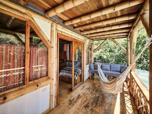 A wooden structure with a covered porch, a hammock, and a bed with pillows. - Bambu Guest House (Santa Cruz La Laguna)