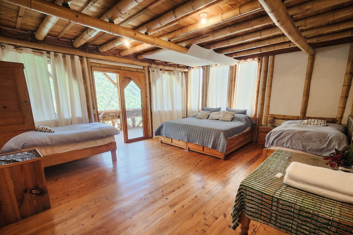 Una habitación con piso de madera, dos camas, un armario de madera y una mesa con una cesta.