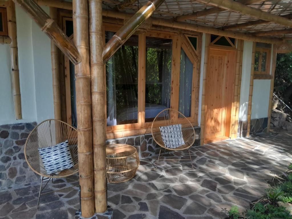 Un área de estar al aire libre techada con piso de piedra, pilares de bambú y mobiliario de mimbre.