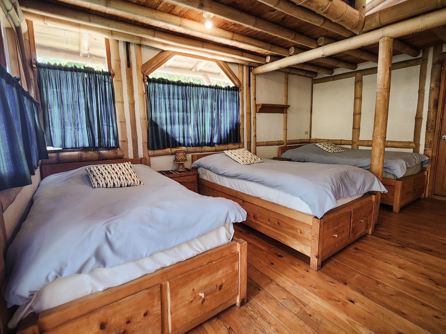Una habitación con dos camas de madera, suelo de madera y estructura de techo de bambú.