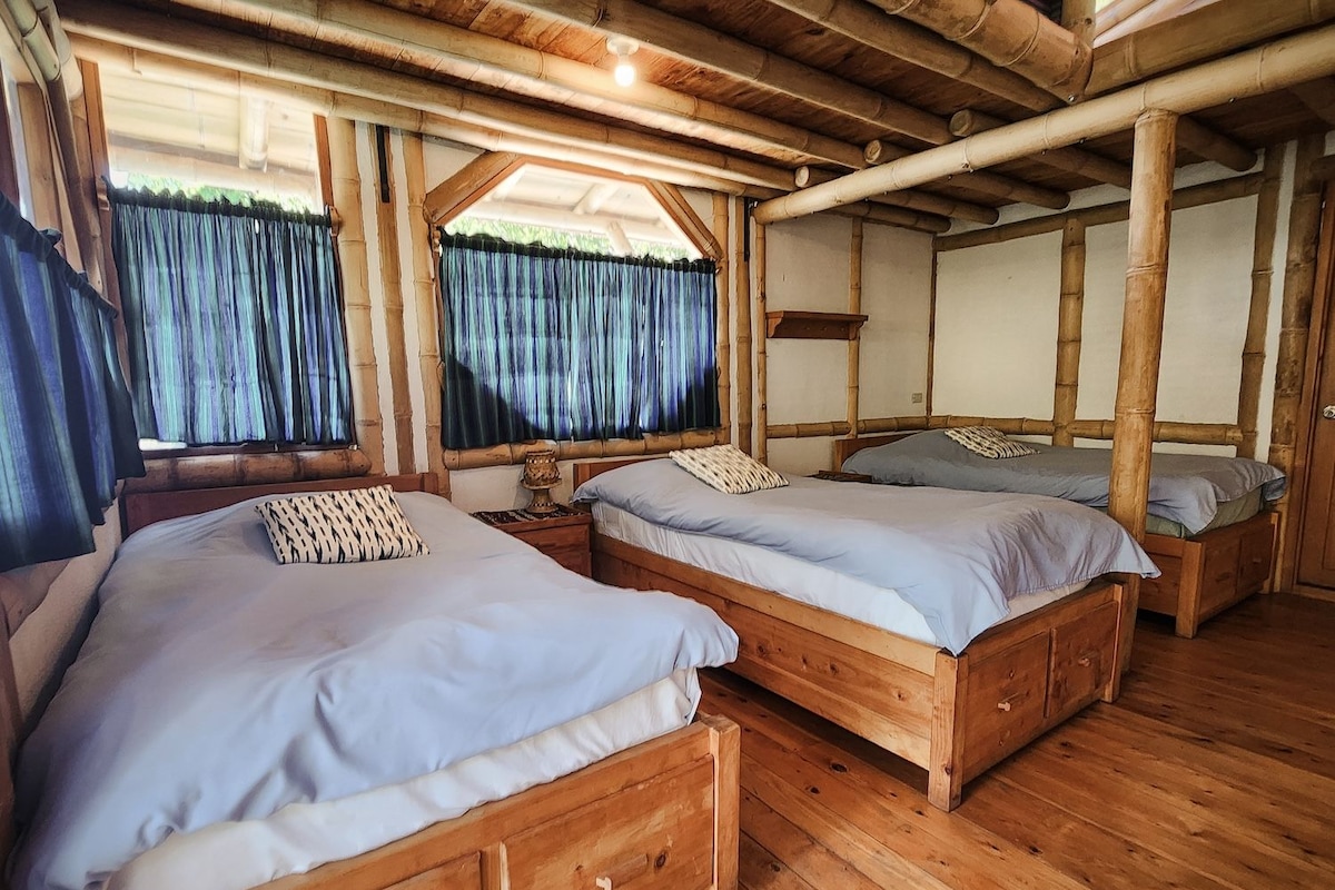 Una habitación con dos camas de madera, suelo de madera y estructura de techo de bambú.