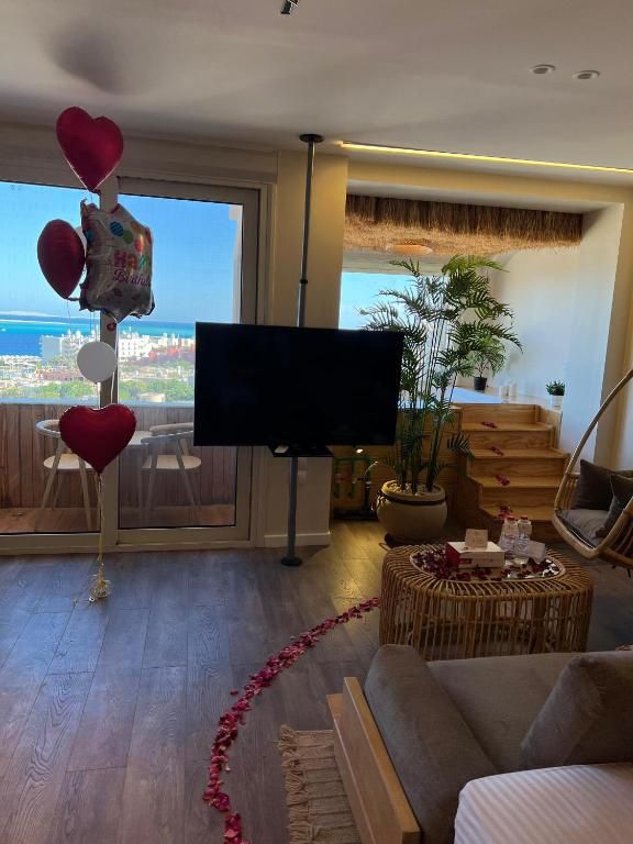Una sala de estar con televisor, un sofá, un comedor con sillas, una planta y vistas a la ciudad.