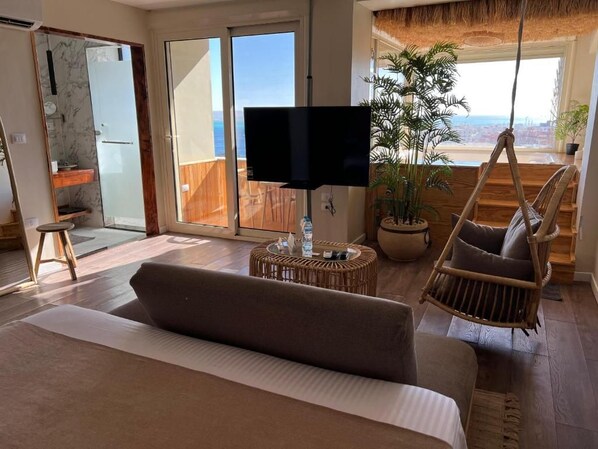 Un dormitorio con cama, televisión, planta en maceta, silla de mimbre y vistas al exterior.
