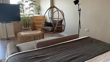 Una habitación moderna con cama, una silla colgante, una mesita redonda y un televisor.