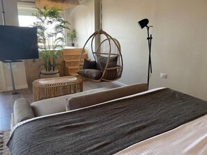 Een moderne kamer met een bed, een hangstoel, een klein rond tafeltje en een televisie.