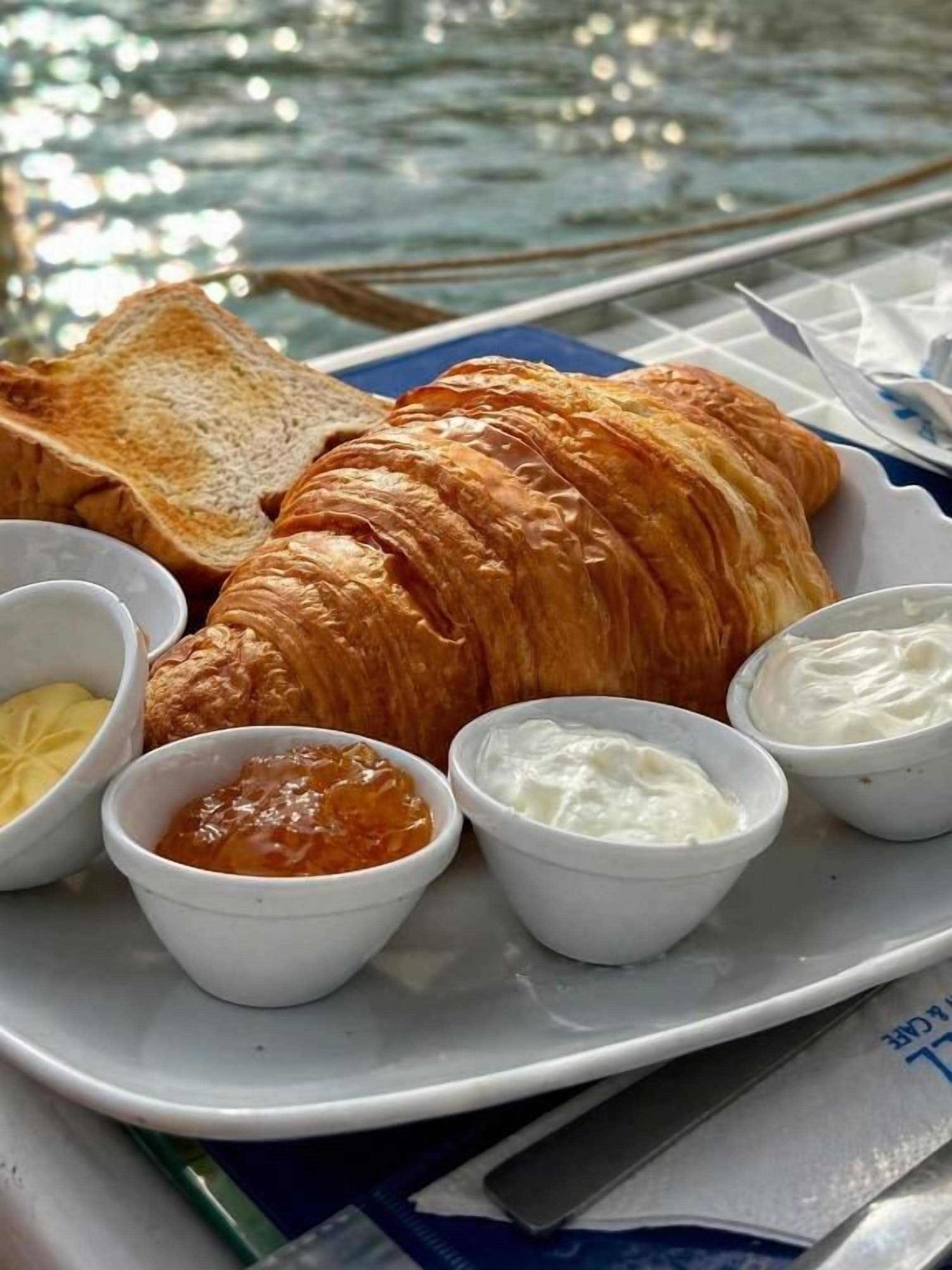 A tray with a croissant, toast, and three small bowls of spreads.